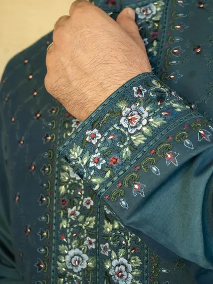 We ensure every part of the garment is a work of art, as seen in the detailed floral embroidery on the cuff of this teal jacket.