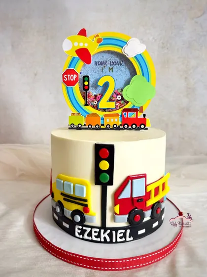 Honk honk, beep beep! A transportation-themed cake for a 2nd birthday, featuring a bus, fire truck, train, and a fun shaker topper with confetti.