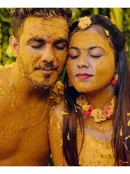 A quiet, intimate moment amidst the Haldi celebration. The couple, covered in turmeric and flower petals, share a peaceful moment with their eyes closed.