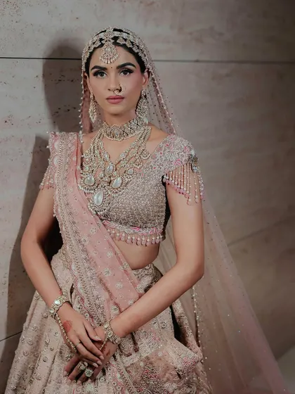 A detailed look at Manisha's bridal ensemble. The pastel pink lehenga is paired with layered diamond necklaces and a matching matha patti, creating a soft yet regal look.