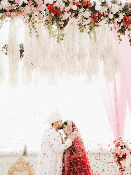 A destination wedding dream realized. Under a canopy of flowers on a serene beach, the groom kisses his bride's forehead, a perfect, timeless moment framed against the vastness of the sea.