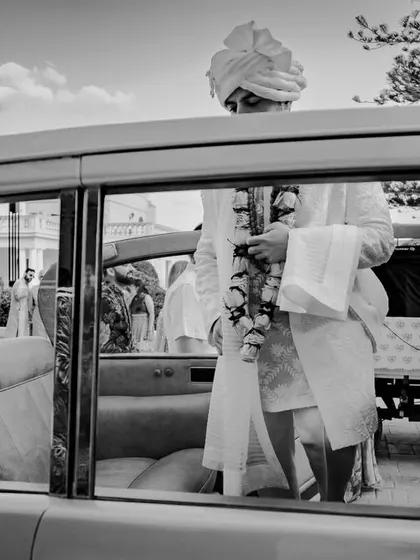 A classic black and white shot of the groom arriving in a vintage car in Malta, capturing a moment of anticipation and timeless style.