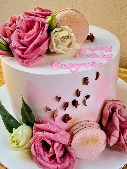 Pink and white roses, macarons and rose petals finish our pale floral birthday cake, with the birthday message piped on top.