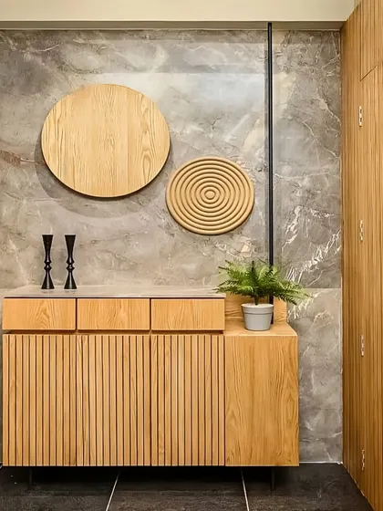 This entryway features a fluted wooden console against a grey marble wall. The circular wooden art pieces add a sculptural element, creating a sophisticated and modern aesthetic right at the entrance.