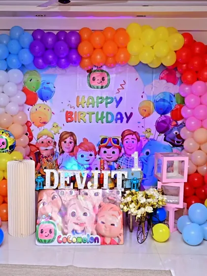 A full and vibrant Cocomelon themed setup for Devjit's birthday at home. The rainbow balloon arch frames the backdrop perfectly, creating a fantastic photo zone.
