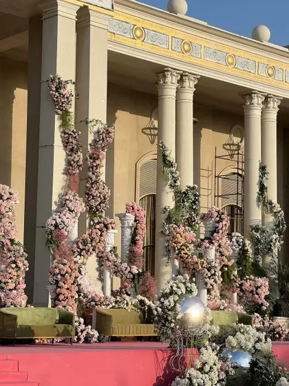 The essence of romance blossoms in every corner. This cocktail night stage features columns entwined with pink and white florals, set against a grand palace, where dreams become reality and every moment is adorned with splendor.