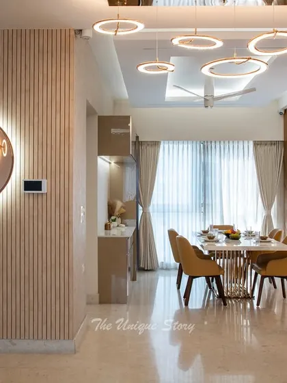 This dining area is a study in modern luxury, featuring a stone-top table with a sculptural golden base and tan leather chairs. The space is illuminated by a series of modern LED ring lights, with a fluted wall panel and a large mirror adding texture and depth.