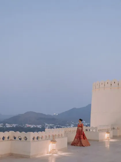 A wide-angle shot of the bride standing alone on a palace rooftop at dusk. The soft evening light and the expansive view of Udaipur create a feeling of peaceful solitude and breathtaking beauty.