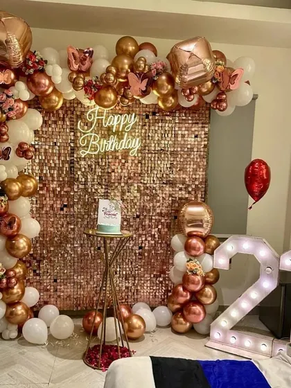A glamorous 21st birthday setup designed for stunning photos. This decoration features a dazzling rose gold sequin wall, a custom neon sign, and an organic balloon arch in rose gold and white, complemented by large '21' marquee lights.