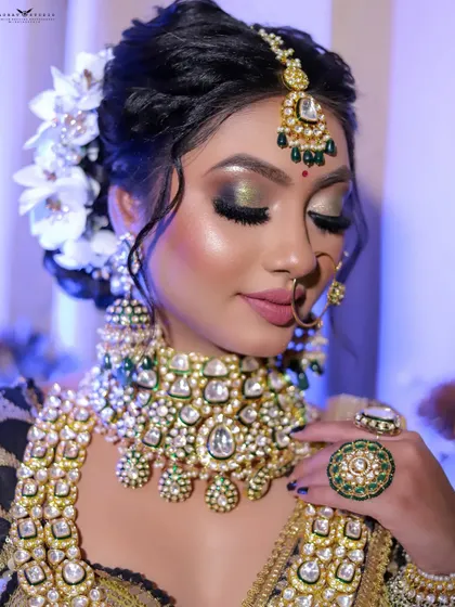 A serene portrait with the bride's eyes closed, showcasing her shimmering green and gold eyeshadow. The pose highlights her intricate ring and floral hair accessory.
