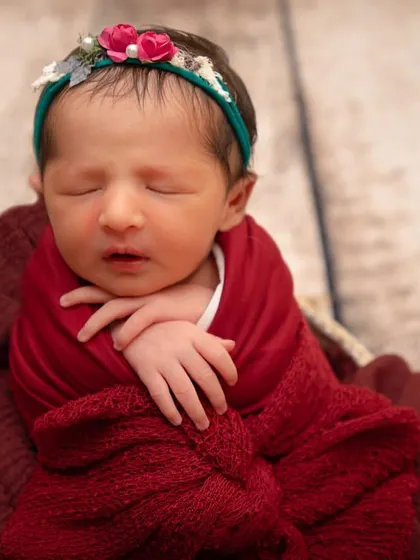 Pure love. This close-up captures the delicate hands and face of a newborn wrapped in a rich red swaddle, looking so peaceful and content.