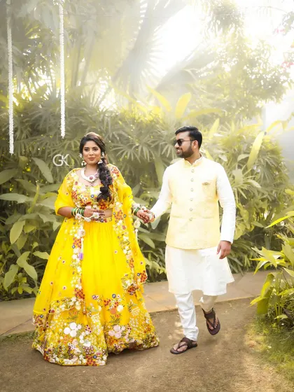The bride and groom walking hand-in-hand. Her vibrant yellow outfit is perfectly complemented by the white and purple floral jewellery we designed.
