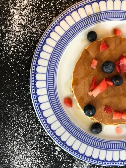 A simple and elegant pancake topped with fresh strawberries and blueberries. The top-down perspective on a decorative plate creates a clean, visually pleasing composition.