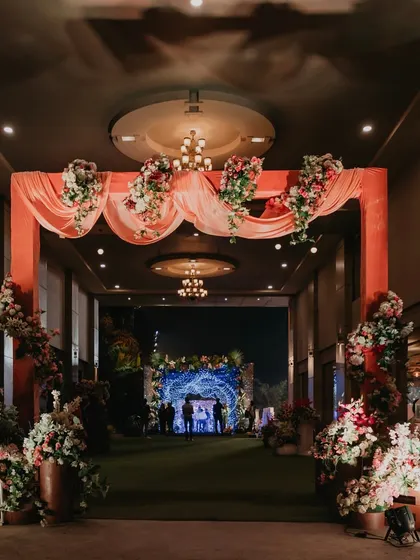 A grand floral entranceway for a sangeet celebration. The combination of soft drapes and lush flower arrangements creates an inviting and elegant welcome for guests.