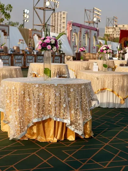 Elegant outdoor table settings for a large reception. The gold-laced tablecloths and simple floral centerpieces create a look of understated luxury.
