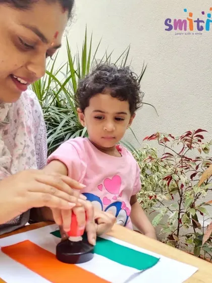 A teacher helps a toddler stamp the Ashoka Chakra onto a handmade flag. We ensure all children, regardless of age, can participate in our national celebrations.