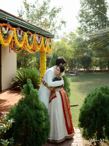 A beautiful, candid embrace between the couple in a garden setting, with traditional marigold decorations in the background. A perfect blend of intimacy and festive atmosphere.