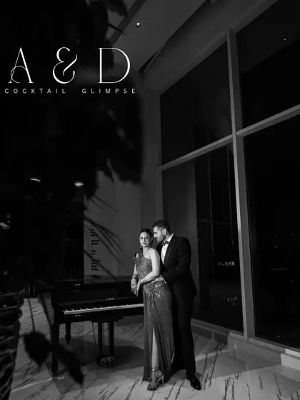 A sophisticated black and white portrait of the couple by a grand piano, looking like they stepped out of a classic film.