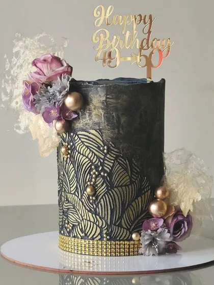 A sophisticated cake perfect for a milestone birthday. I created a dark, moody base and overlaid it with a gold leaf-patterned stencil, adding texture with edible pearls and delicate rice paper sails.