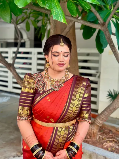 A beautiful bride in a traditional red and maroon saree. Her makeup is classic and elegant, with soft smokey eyes and a neutral lip color that complements her rich attire.