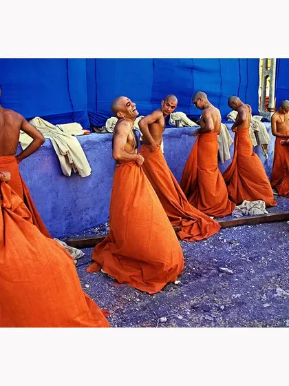 A candid moment of joy and camaraderie among young Buddhist monks. The vibrant orange of their robes against the stark blue wall creates a powerful color contrast, highlighting a moment of uninhibited laughter.
