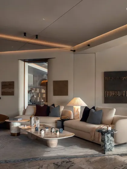 The living room at Palais Royale, where a sculptural coffee table and curved sofas anchor the room. The design's organic silhouettes add drama, while the soft glow of ambient lighting enhances the subtle veining of the marble flooring.
