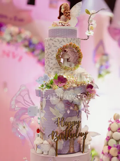 An incredibly detailed, multi-tiered birthday cake for the fairytale party, adorned with delicate sugar flowers, fairies, and woodland elements.
