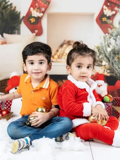 Two siblings sit together in a Christmas setup, holding golden ornaments. A perfect holiday card photo.
