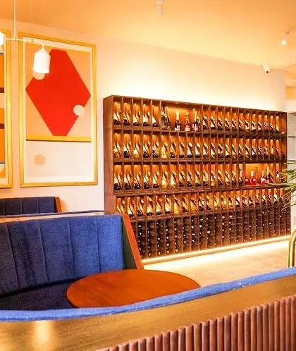 The interior of Haute, a wine bar we designed in Indiranagar, Bengaluru. The space features plush booth seating, a prominent wine display, and bold artwork to create a sophisticated and inviting atmosphere.