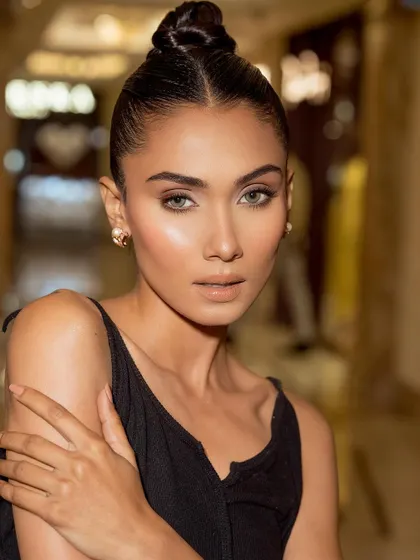 A candid-style portrait of a model at a DLF Emporio masterclass. The look is pure summer glam, with dewy skin, a nude lip, and a sleek top knot, captured with soft, ambient light.