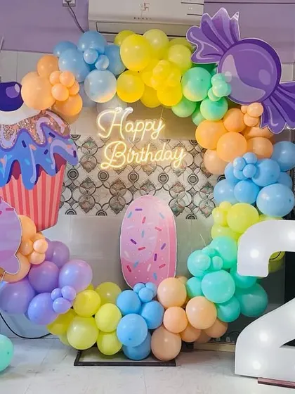 A delicious-looking candyland themed second birthday. The decor features a colorful balloon ring with large cutouts of an ice cream cone, a cupcake, and candy.