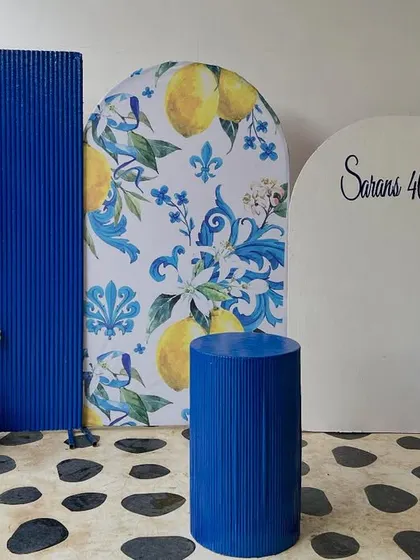 A full view of the Amalfi-themed setup for Saran's 40th birthday. We combined a custom lemon-print arch, a bold blue textured panel, and a personalized white arch with a fun balloon garland.