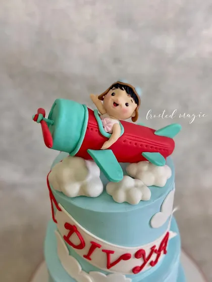 Look at this little pilot waving from her aeroplane! This handmade fondant topper was created for a second birthday, showing that even the smallest details, like the cute expression, are crafted with love to make the cake special.