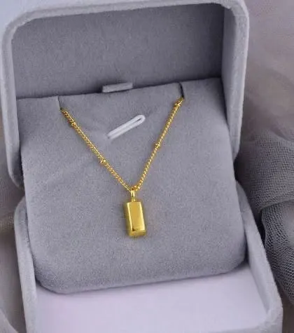 A minimalist necklace featuring a small, gold bar pendant on a delicate beaded chain. This piece is perfect for a clean, modern look and comes in a soft grey gift box.