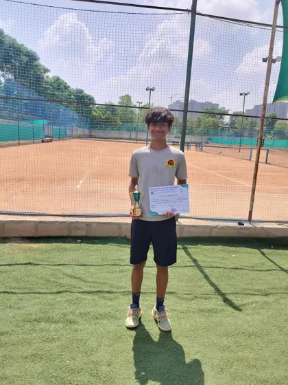 Svar proudly displays his finalist trophy and certificate on the court after the AITA SS U-14 Doubles tournament.