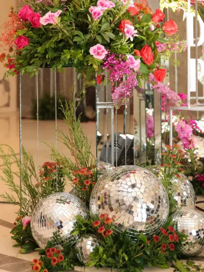 A creative decor element using disco balls of various sizes, nestled in greenery and flowers at the base of a mirrored pedestal.