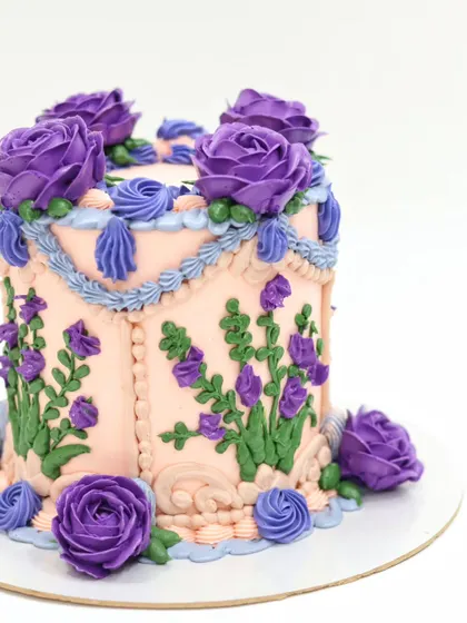 A side view of the purple and peach vintage buttercream cake, highlighting the piped floral swags and shell borders that give it a classic, romantic feel.