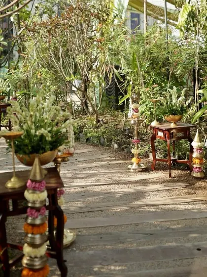 A rustic pathway in a garden venue, lined with traditional floral arrangements and brass lamps.