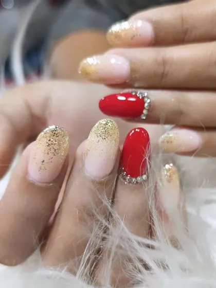 A glamorous party look combining red nails with rhinestone borders and a sparkling gold glitter ombre.