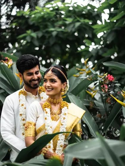 A smiling portrait of the couple amidst tropical plants. The natural setting adds a fresh and vibrant feel to this South Indian wedding photo.