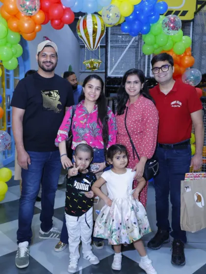 A family poses in front of a colorful balloon arch, celebrating a special day.