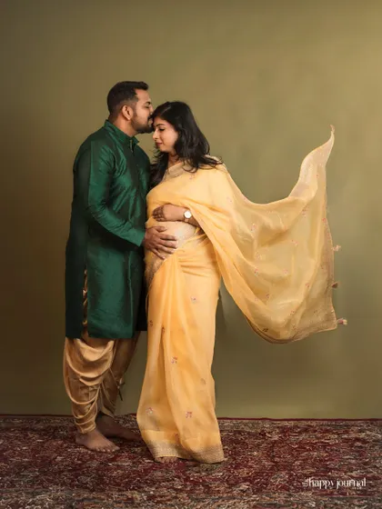 A tender kiss for his wife and their coming baby. This image captures the love and support between partners during a traditional maternity session, set against a classic studio backdrop.