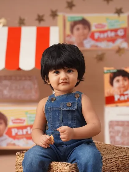 A close-up portrait for a nostalgic Parle-G themed first birthday shoot, with the baby girl in denim overalls looking just like the iconic biscuit brand's mascot.