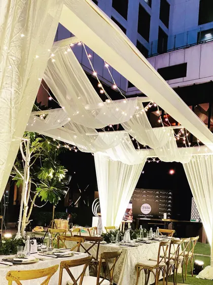 An intimate dinner setting under a canopy of sheer white drapes and twinkling fairy lights, creating a magical, starlit atmosphere for a private party.