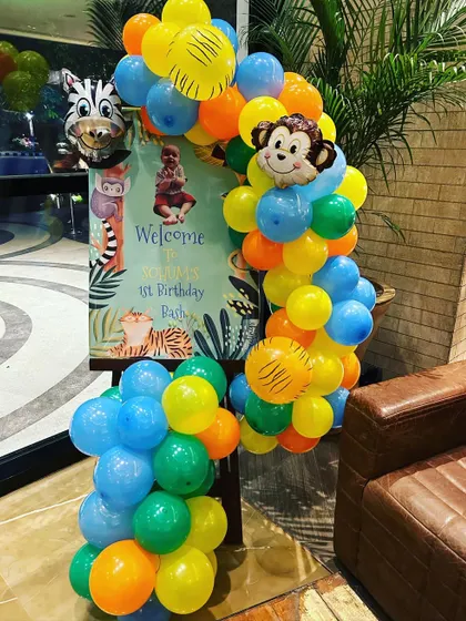 A personalized welcome sign for a jungle-themed first birthday. The sign is framed by a colorful balloon arrangement with monkey and zebra foil balloons.