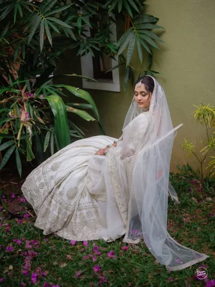 A tranquil portrait of the bride seated in a garden, her white lehenga and veil creating a beautiful contrast with the surrounding greenery.