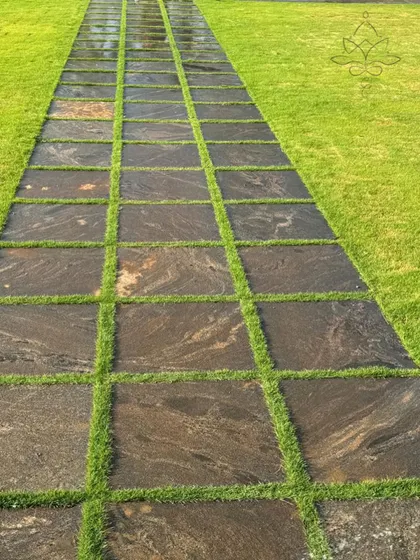 A pathway made of dark, marbled granite tiles with grass joints, offering a sleek and modern look that contrasts beautifully with the bright green lawn.