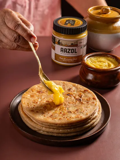 A product shot for a D2C ghee brand, styled in a traditional setting with parathas. This approach connects the product to its cultural roots and usage.