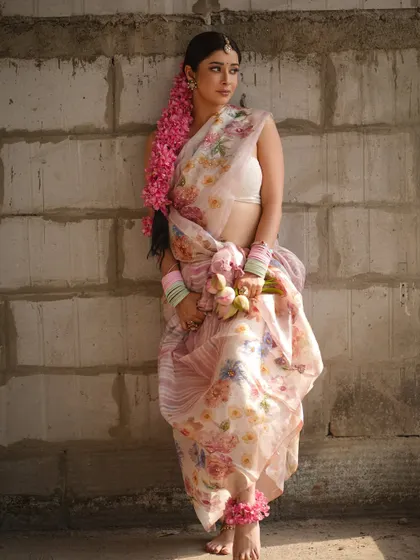 A full-length view of the floral saree look, showing the unique dhoti-style drape. The styling with pastel bangles and a long floral braid creates a fresh, youthful, and rustic aesthetic.