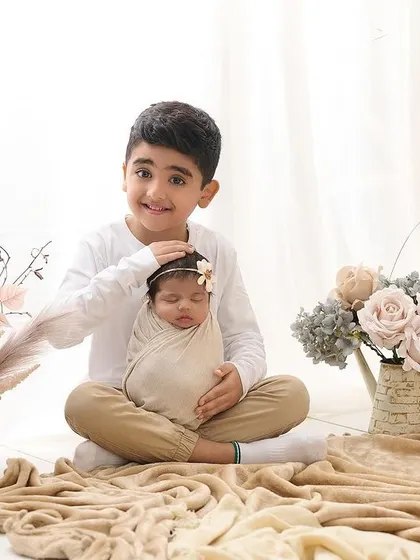 A proud big brother gently holds his newborn sibling. We love capturing these first moments of a new sibling bond in our studio, surrounded by soft, neutral-toned props.